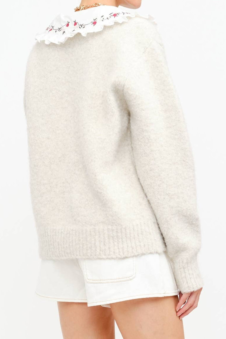 White sweater with floral lace trim worn by a person on a white background