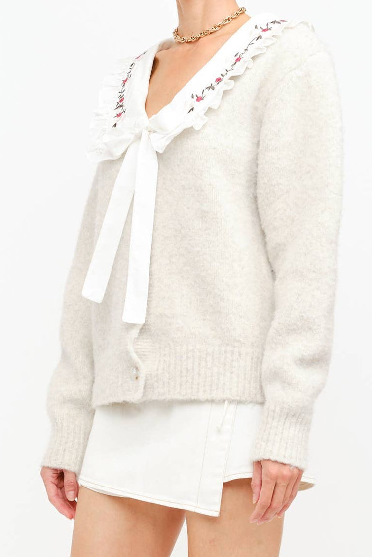 White sweater with a bow tie and floral embroidery on a white background