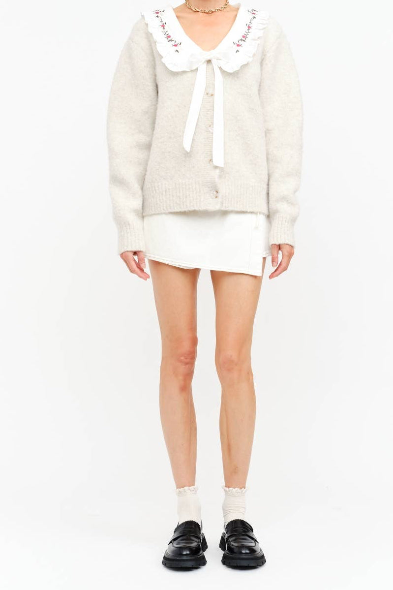 Person wearing a white sweater with lace collar and white skirt on a white background